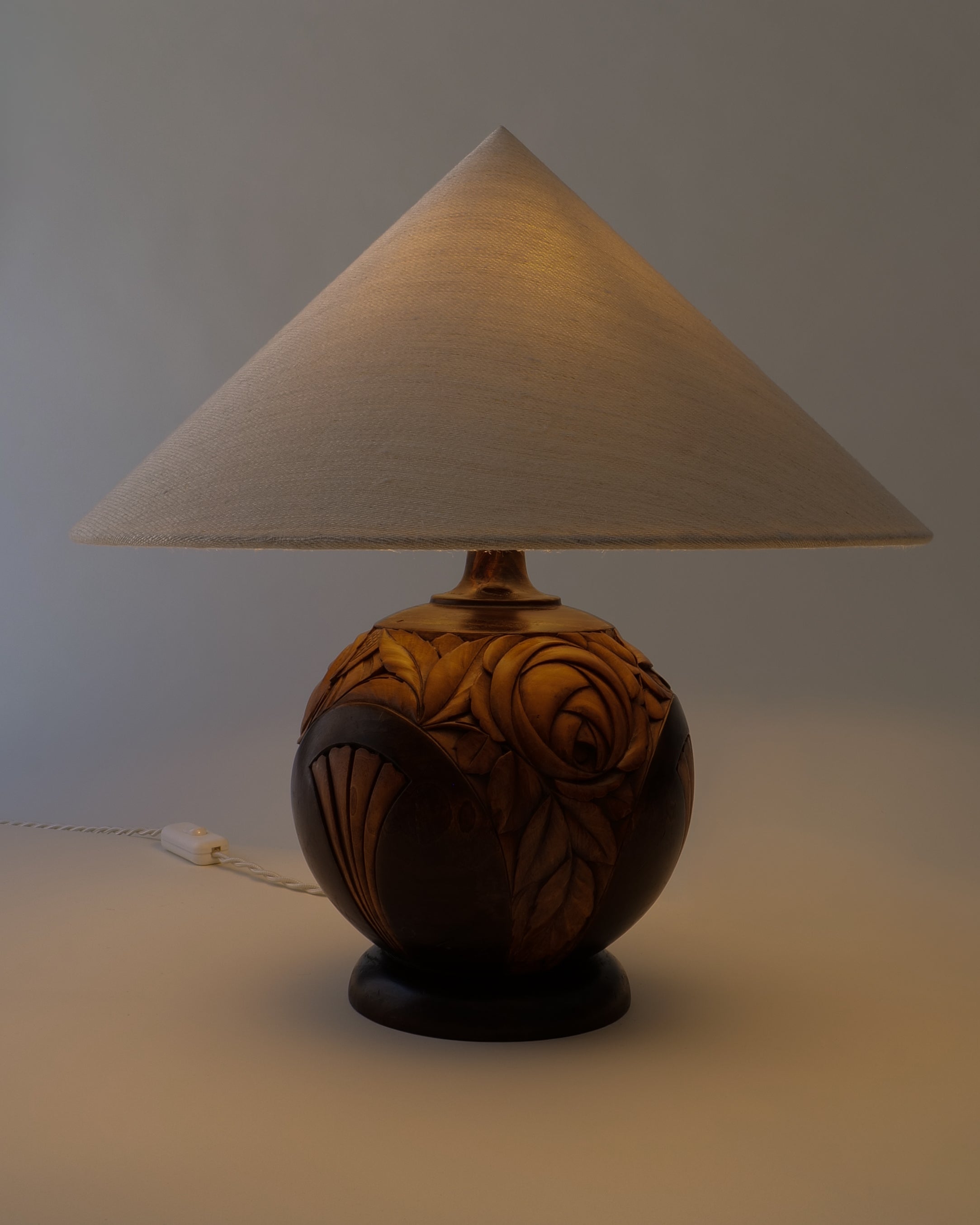  French Art Deco carved walnut table lamp, lit with warm glow, hemp shade illuminated