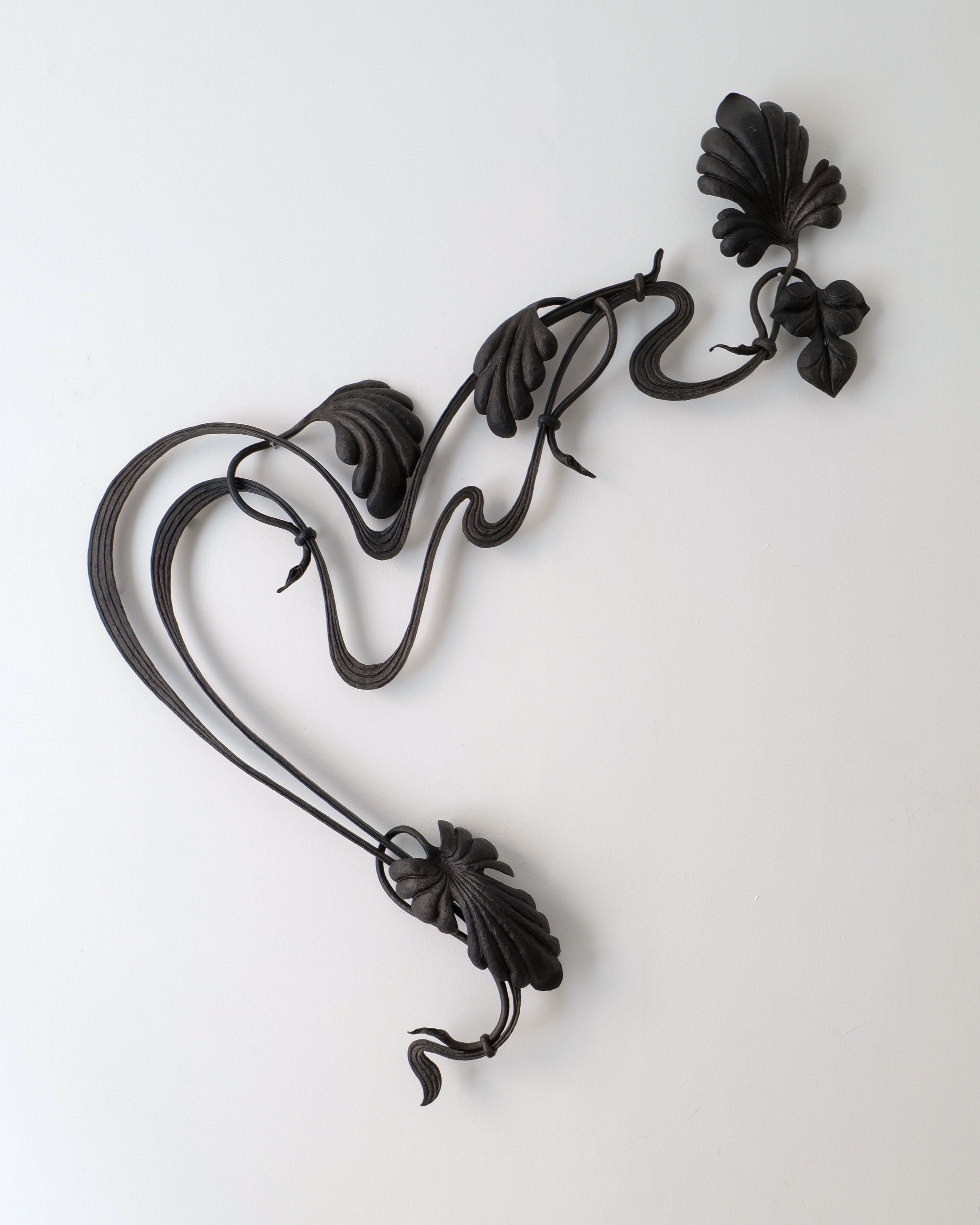 Decorative black metal wall piece with floral designs on a white background