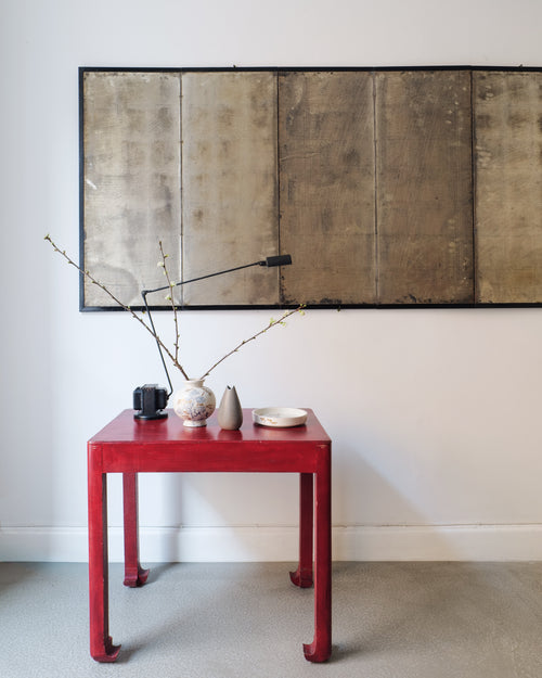 Red table with decorative items against a white wall with a large silver leaf Japanese Screen.