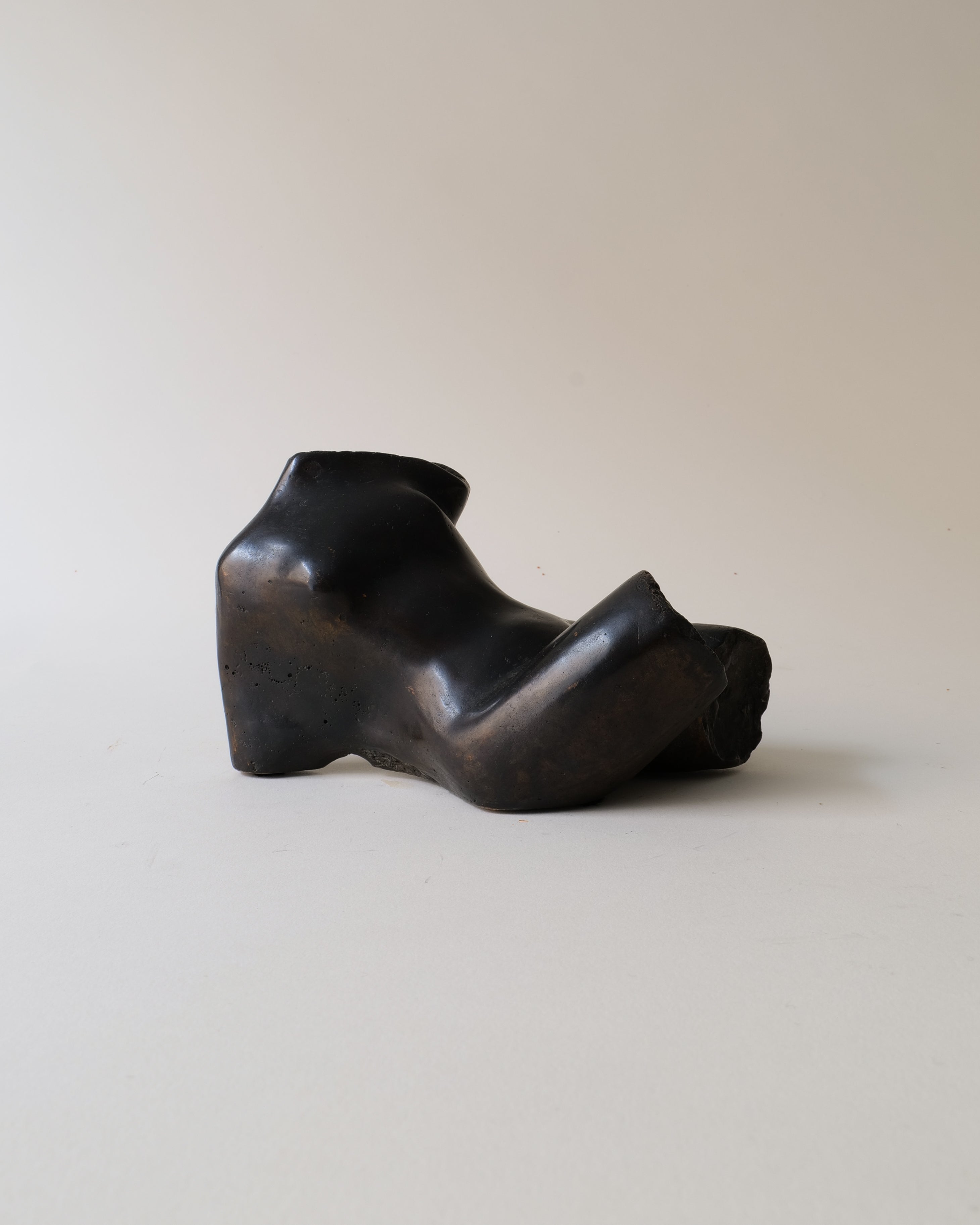 Black bronze sculpture of reclining figure on beige background
