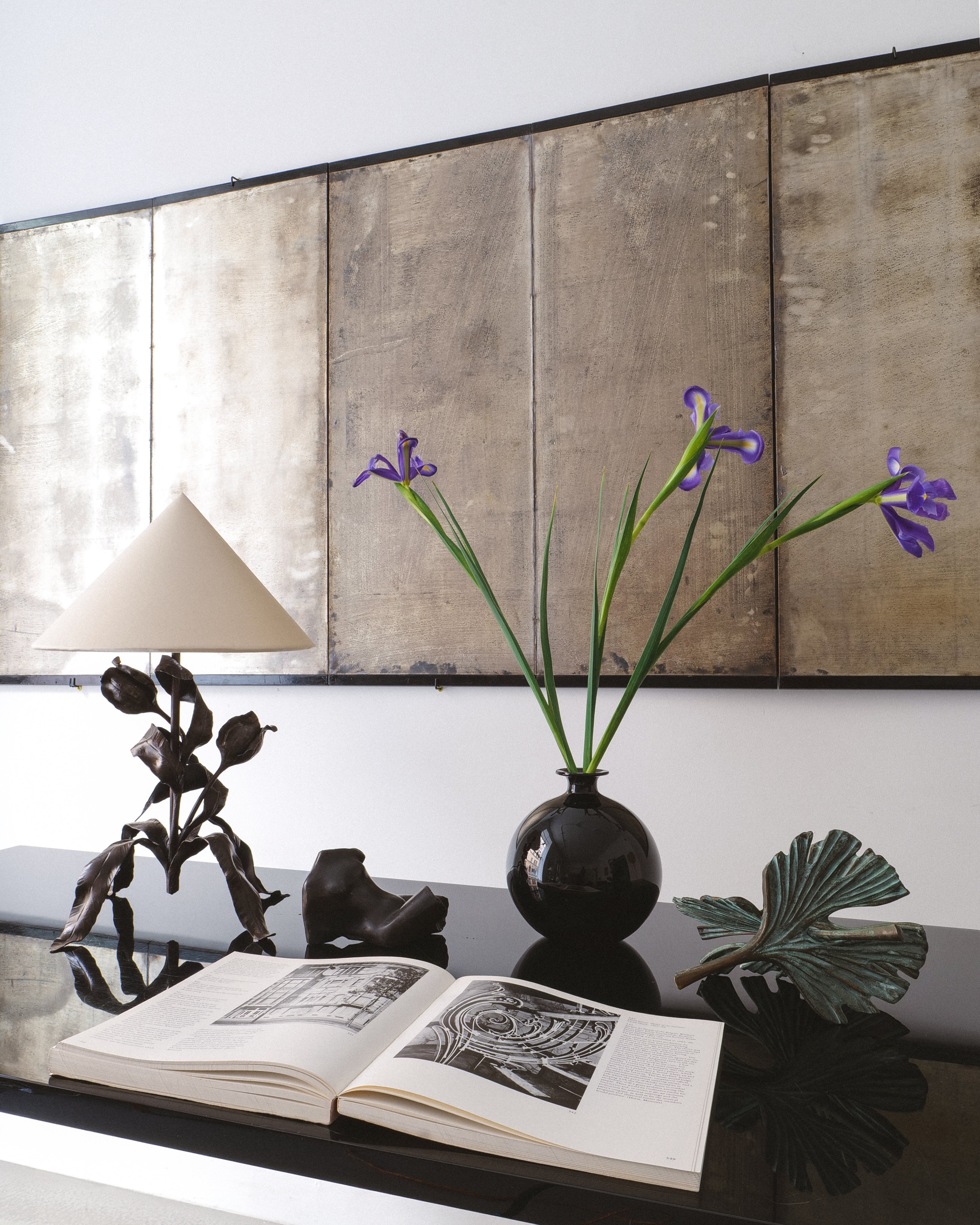 Decorative setup with a vase of flowers, open book, and lamp with  Japanese folding screen with silver leaf in background