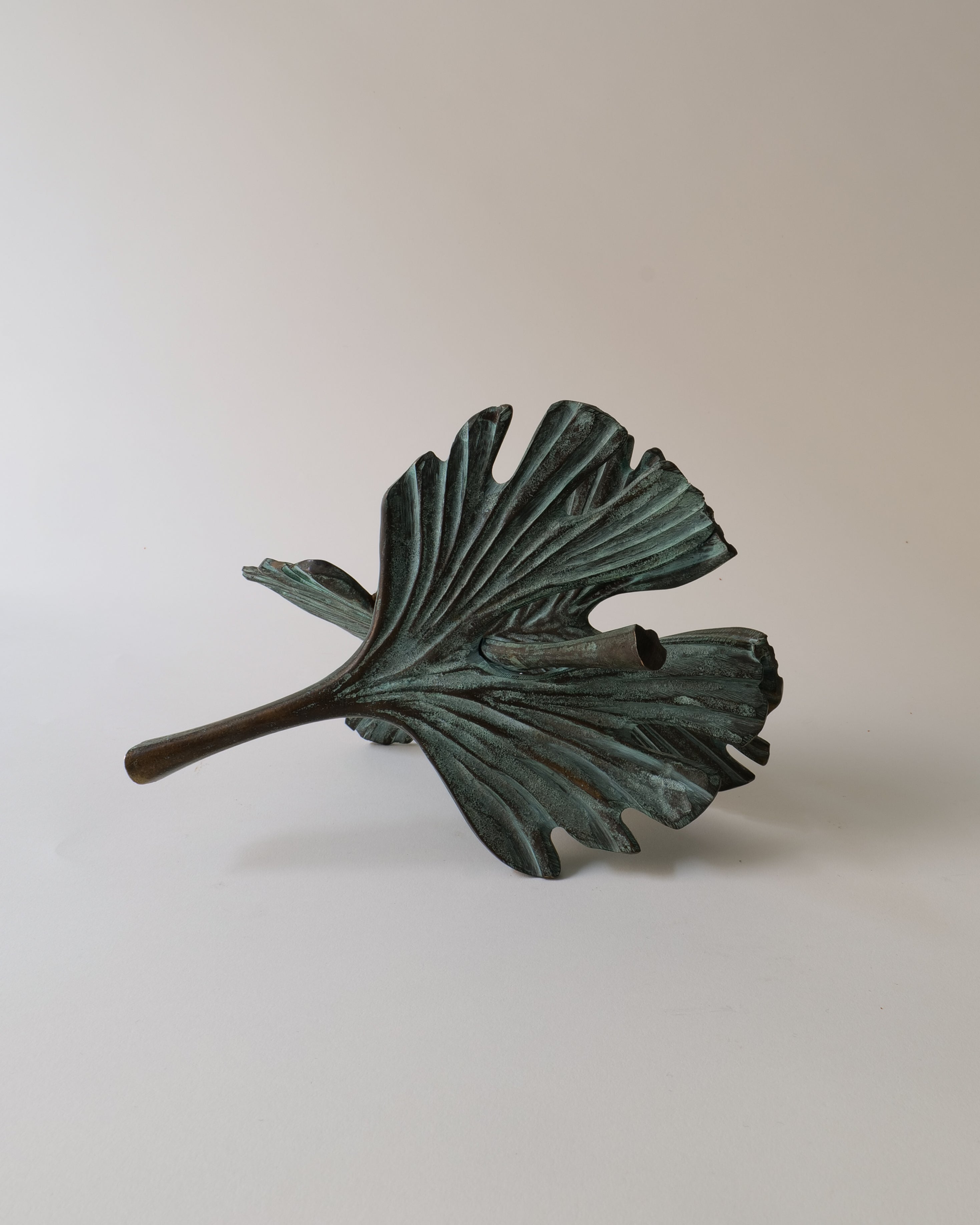 Bronze leaf-shaped sculpture on a light gray background