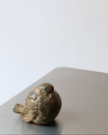 A bronze sculpture of a wren, with a textured surface and a distinctive patina, placed on a reflective metallic surface.