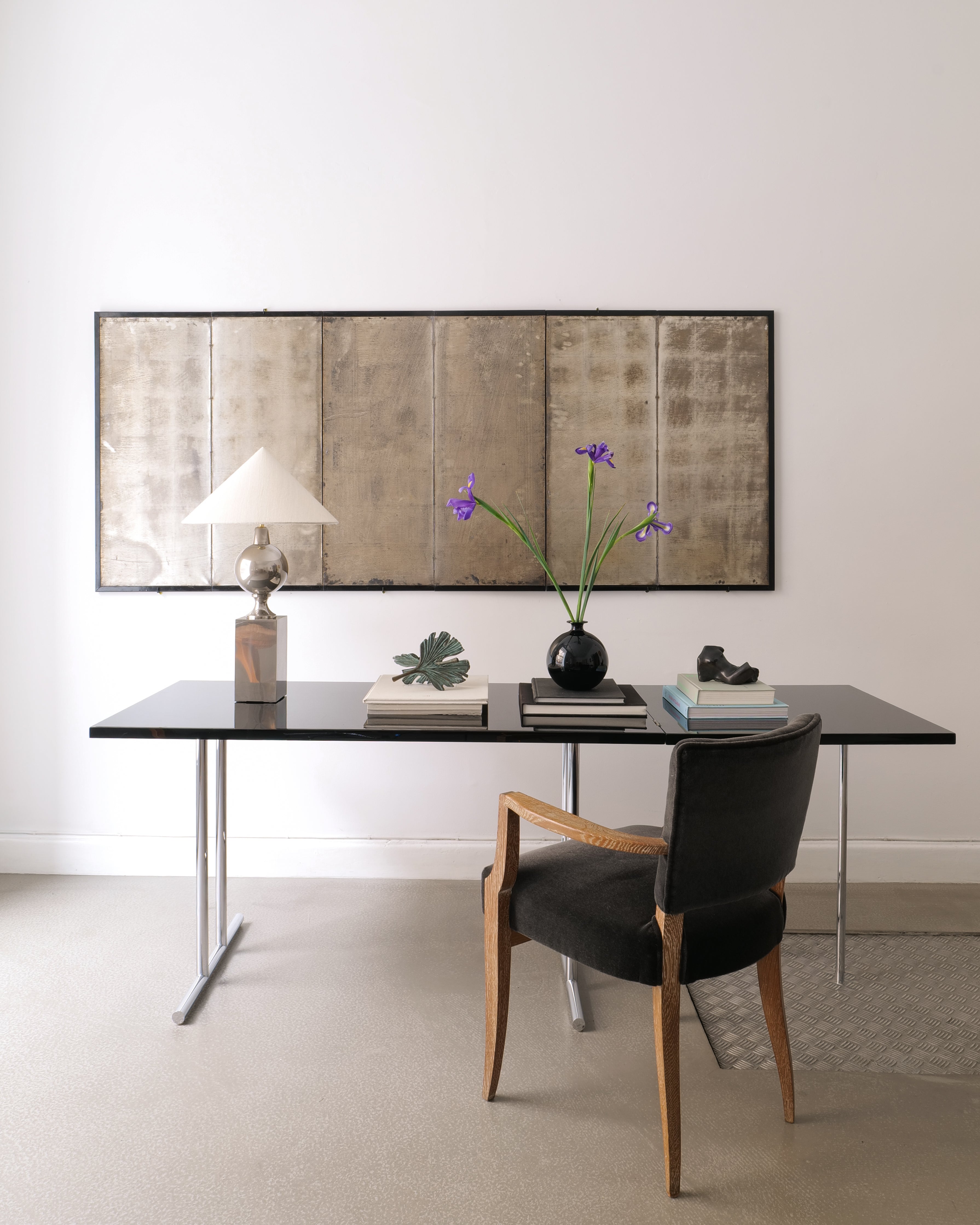 Modern office desk with black top and wooden chair, framed artwork on the wall.