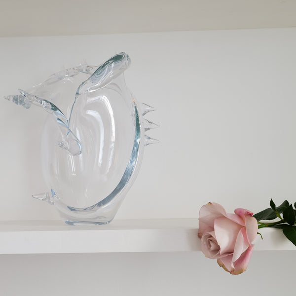 Clear glass vase on a white surface with a pink rose beside it.