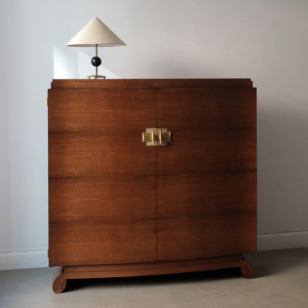 Wooden dresser with a lamp on top against a plain wall