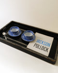 Black Art Deco chinoiserie lacquer tray styled with two blue cups, saucers and a book
