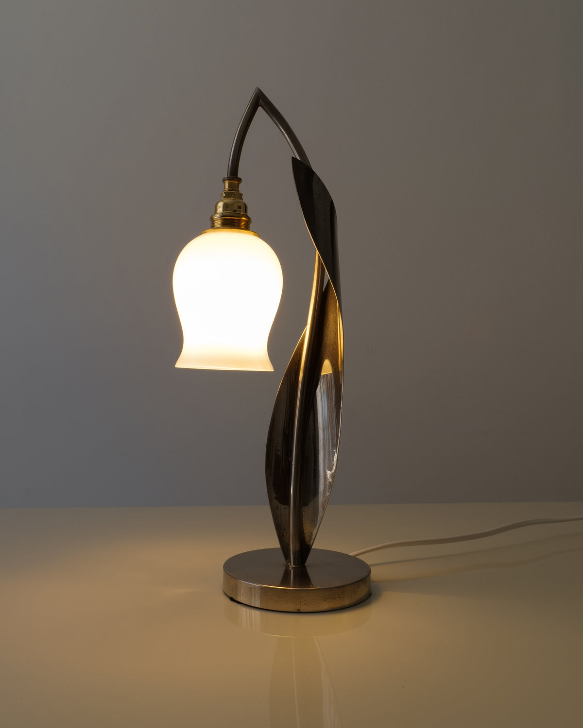 Chrome lily-of-the-valley table lamp illuminated against a dark background
