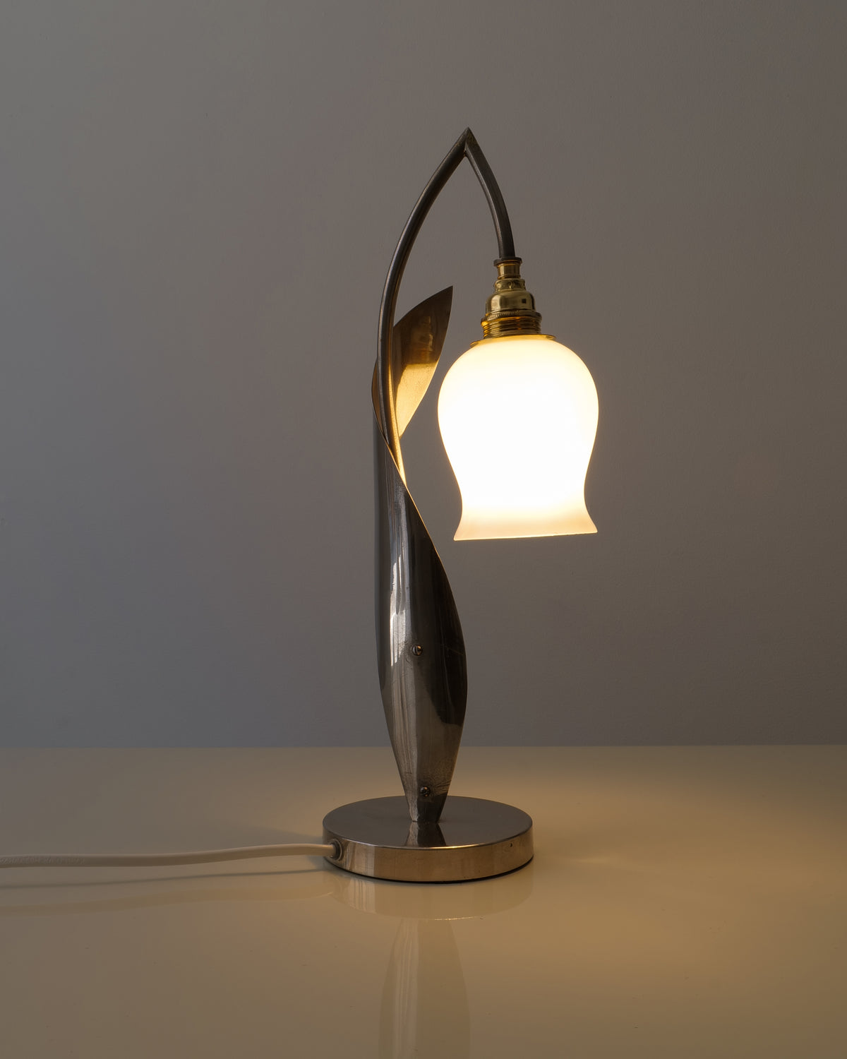 Opaline glass flower shade glowing on the sculptural chrome table lamp

