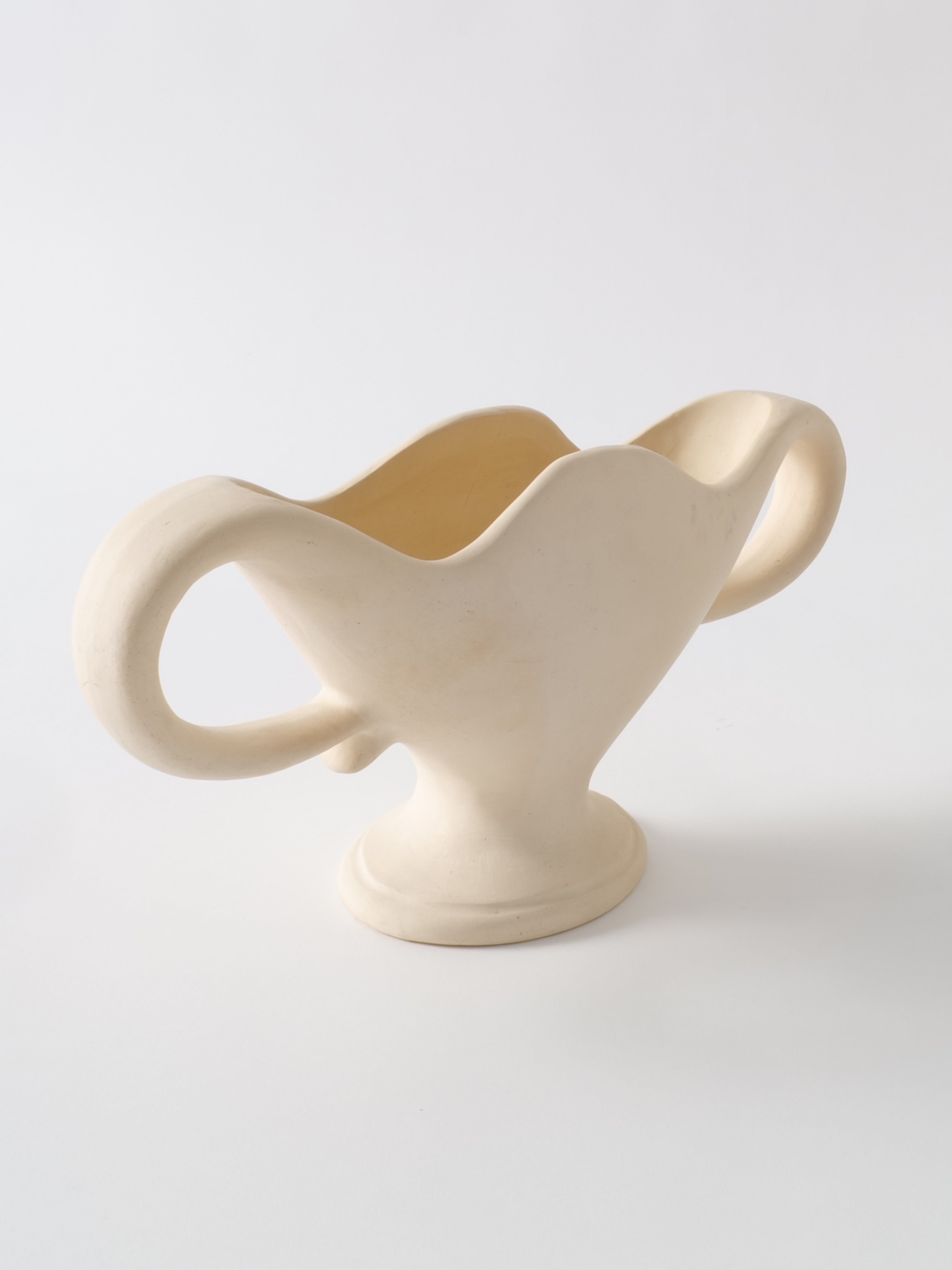 White ceramic vase with undulating handles on white background.