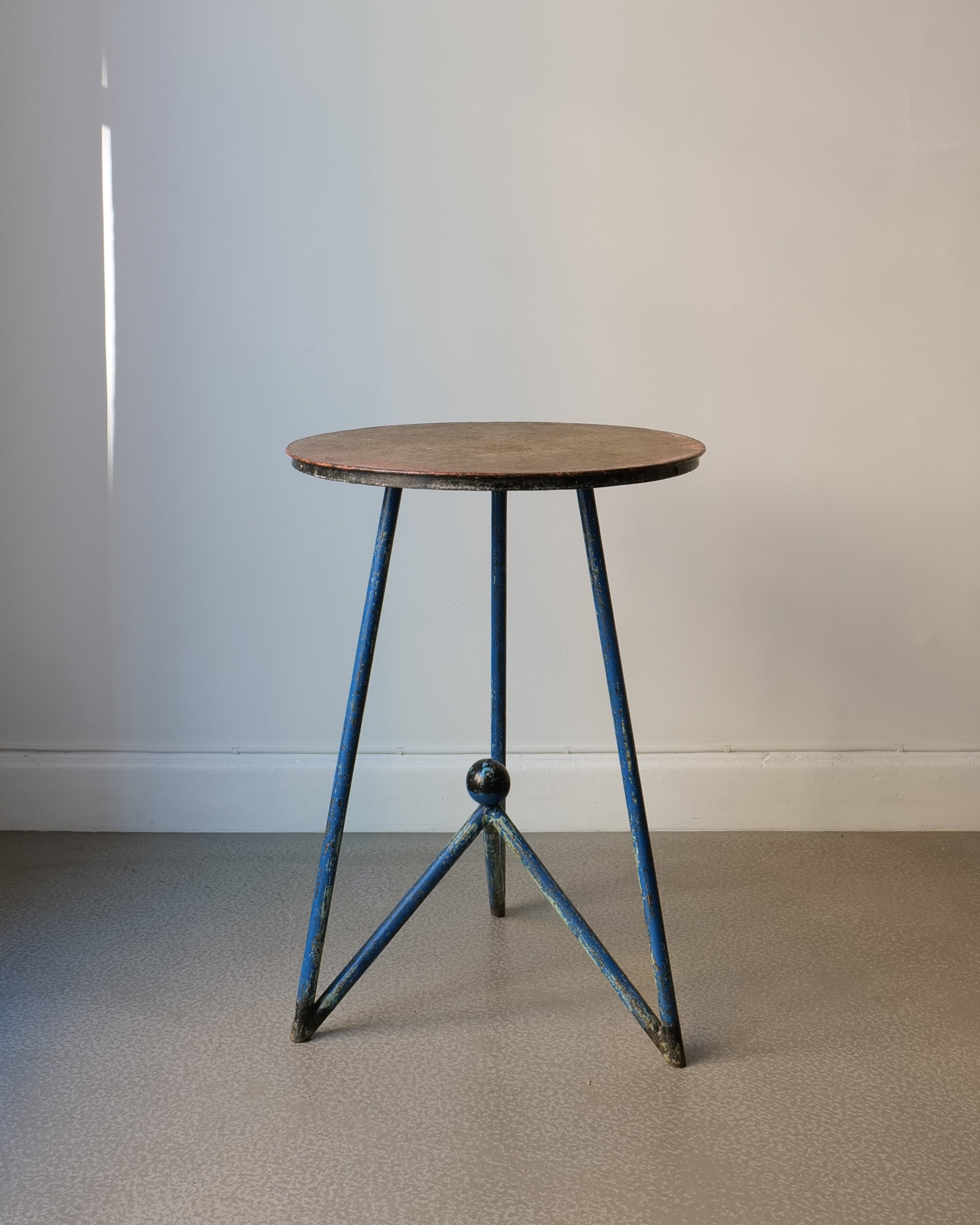 A vintage metal table with a tripod form and a round wooden top, featuring blue painted legs and a patina finish.