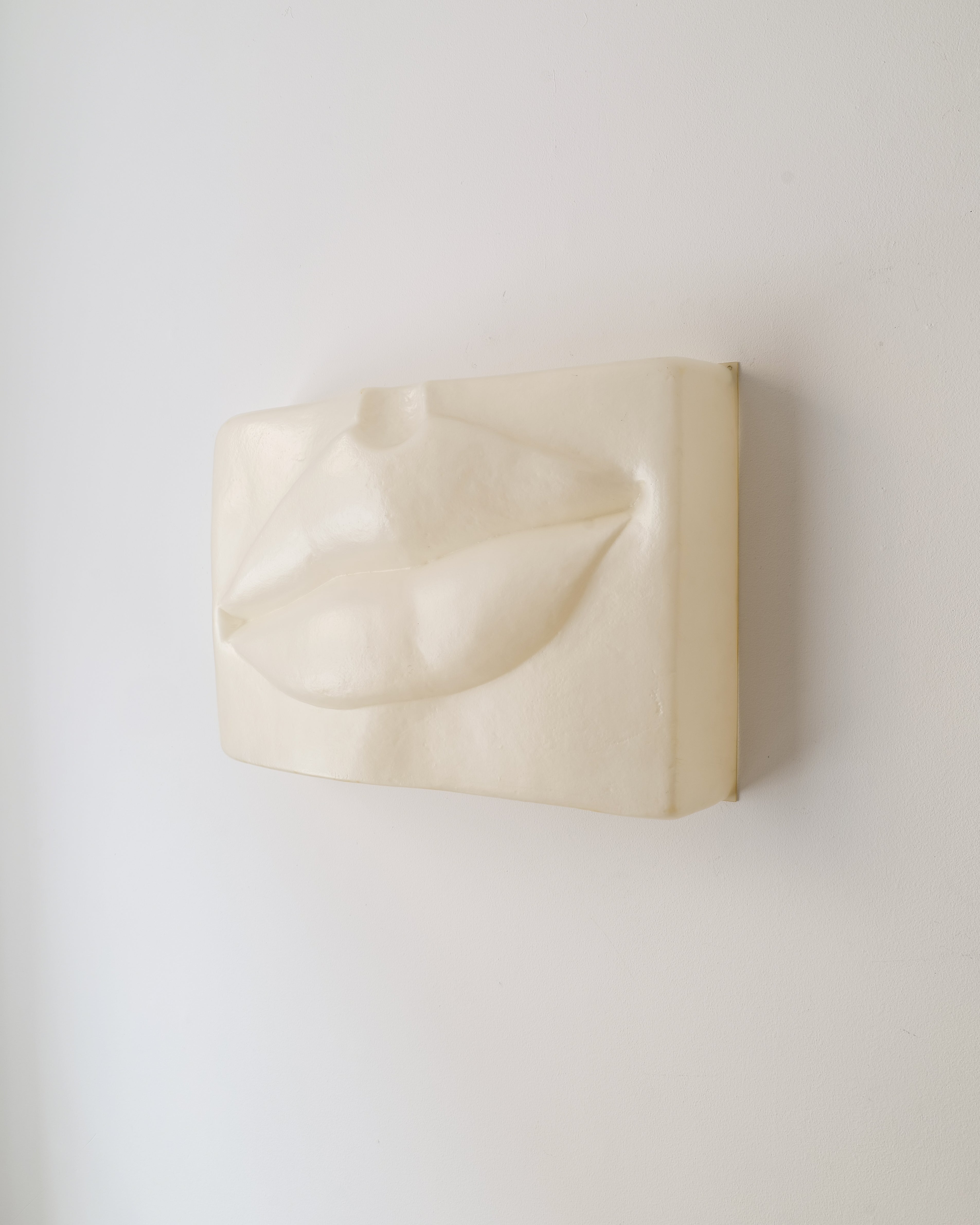 Beige wall sculpture of a mouth form on beige background by Swedish artist Hertha Hillfon.