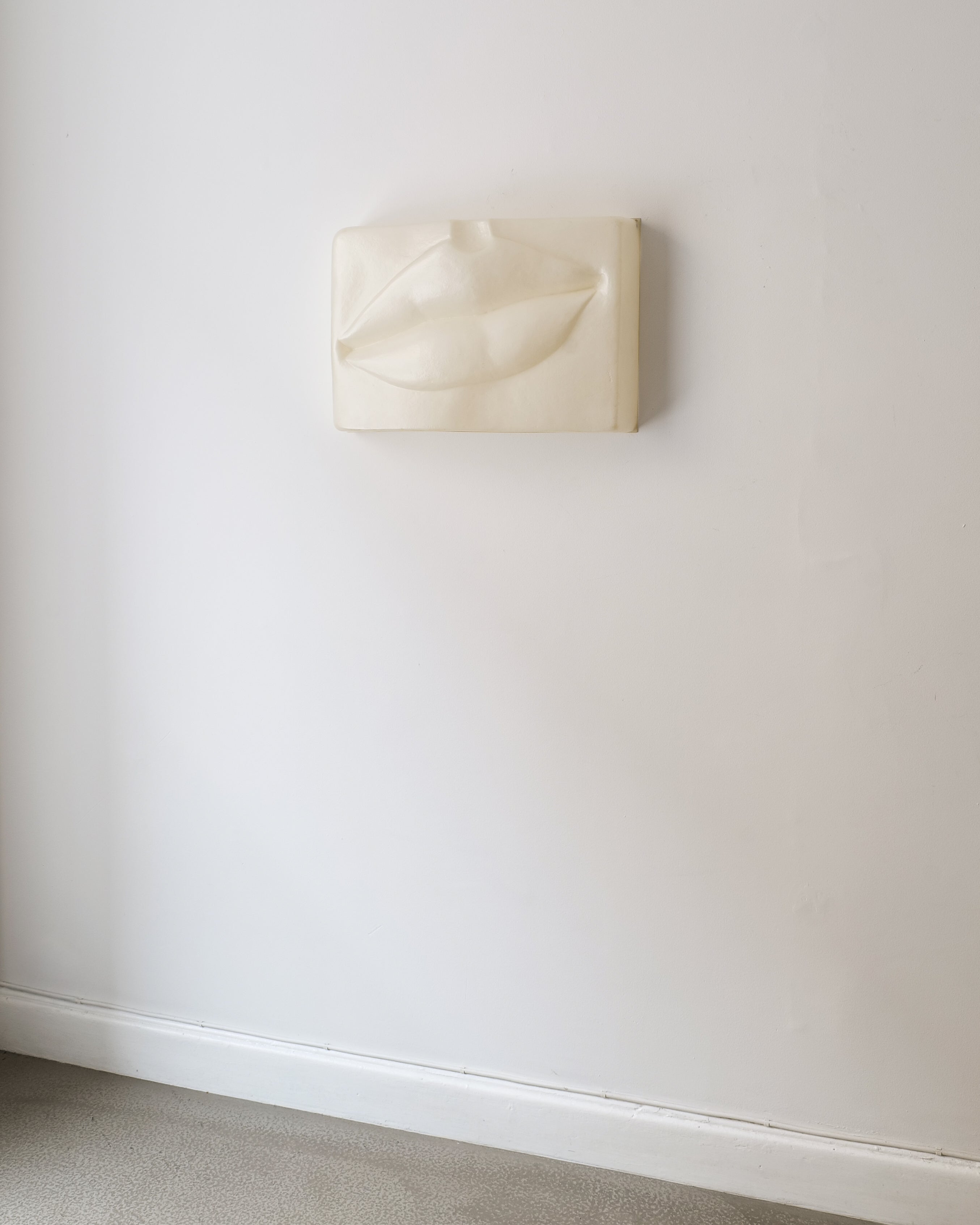 Beige wall sculpture of a mouth form on beige background by Swedish artist Hertha Hillfon.