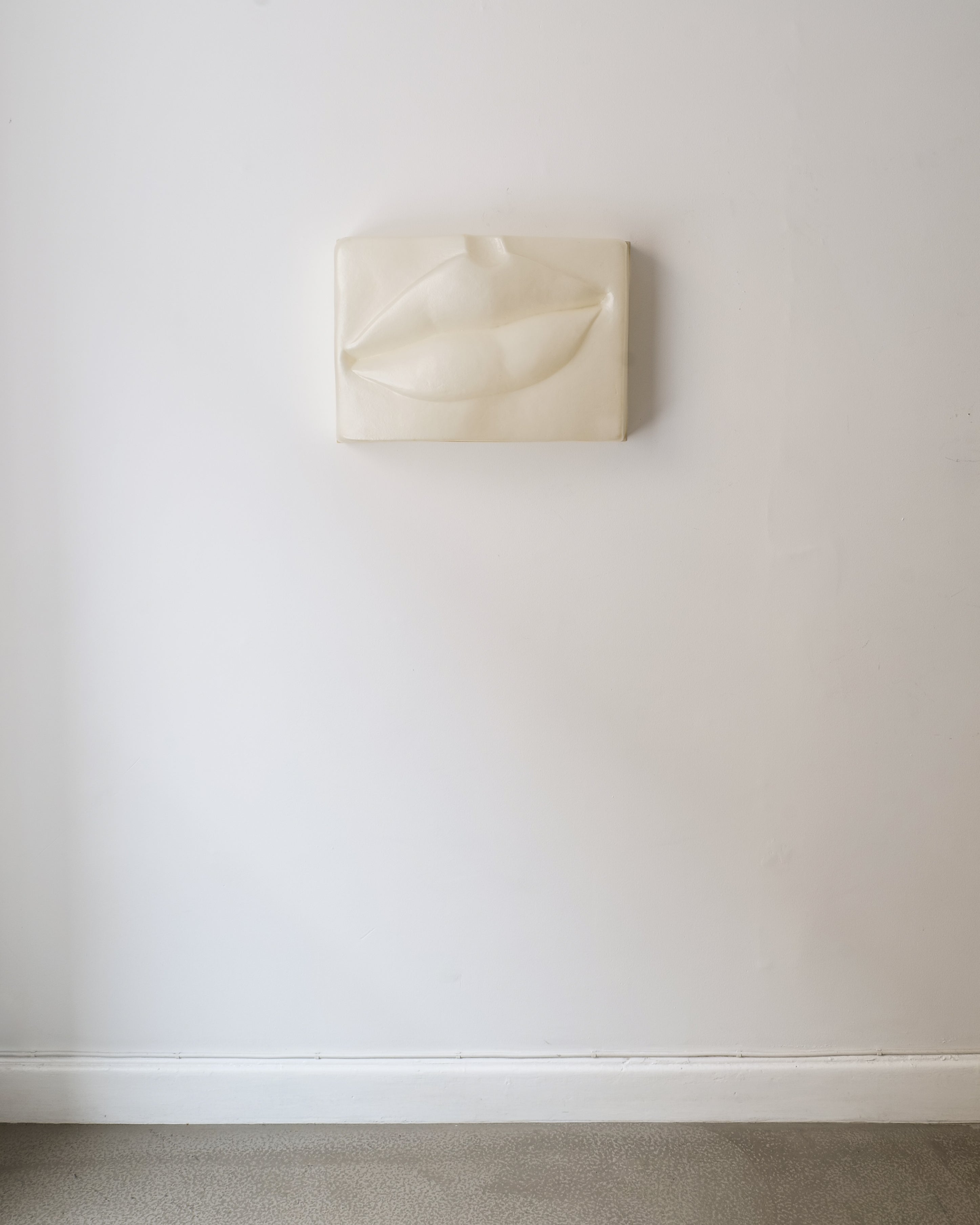 Beige wall sculpture of a mouth form on beige background by Swedish artist Hertha Hillfon.