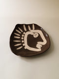 Ceramic dish with a stylized face design on a beige background