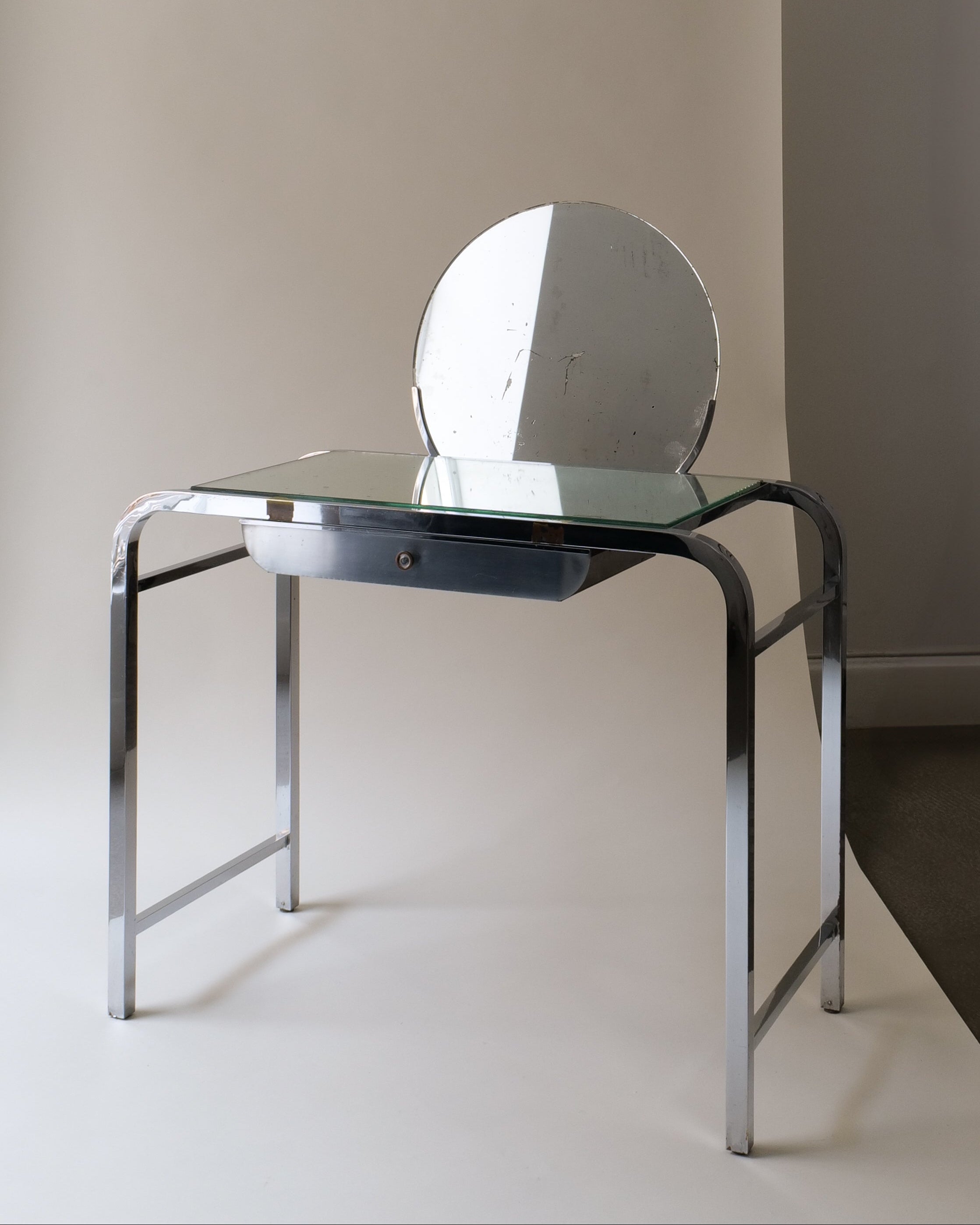 A sleek Modernist French Vanity table with a mirrored rectangular top, hemispherical mirror, and square sectioned legs. Features a central wooden draw with a brass handle and is chrome-plated.