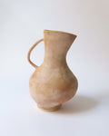 An earth-toned, organically shaped stoneware ceramic pitcher with a textured patina and a handle on the side.
