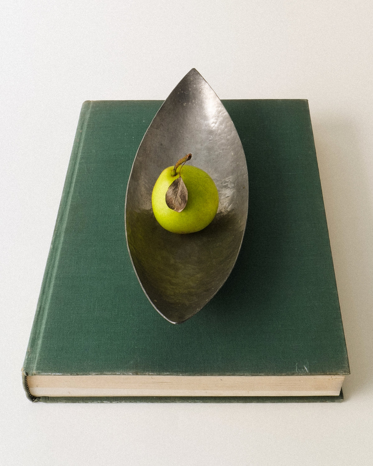 Erik Torssell pewter bowl from 1969 styled with a green apple on a book
