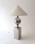 Table lamp with a silver metallic base and white lampshade on a light background