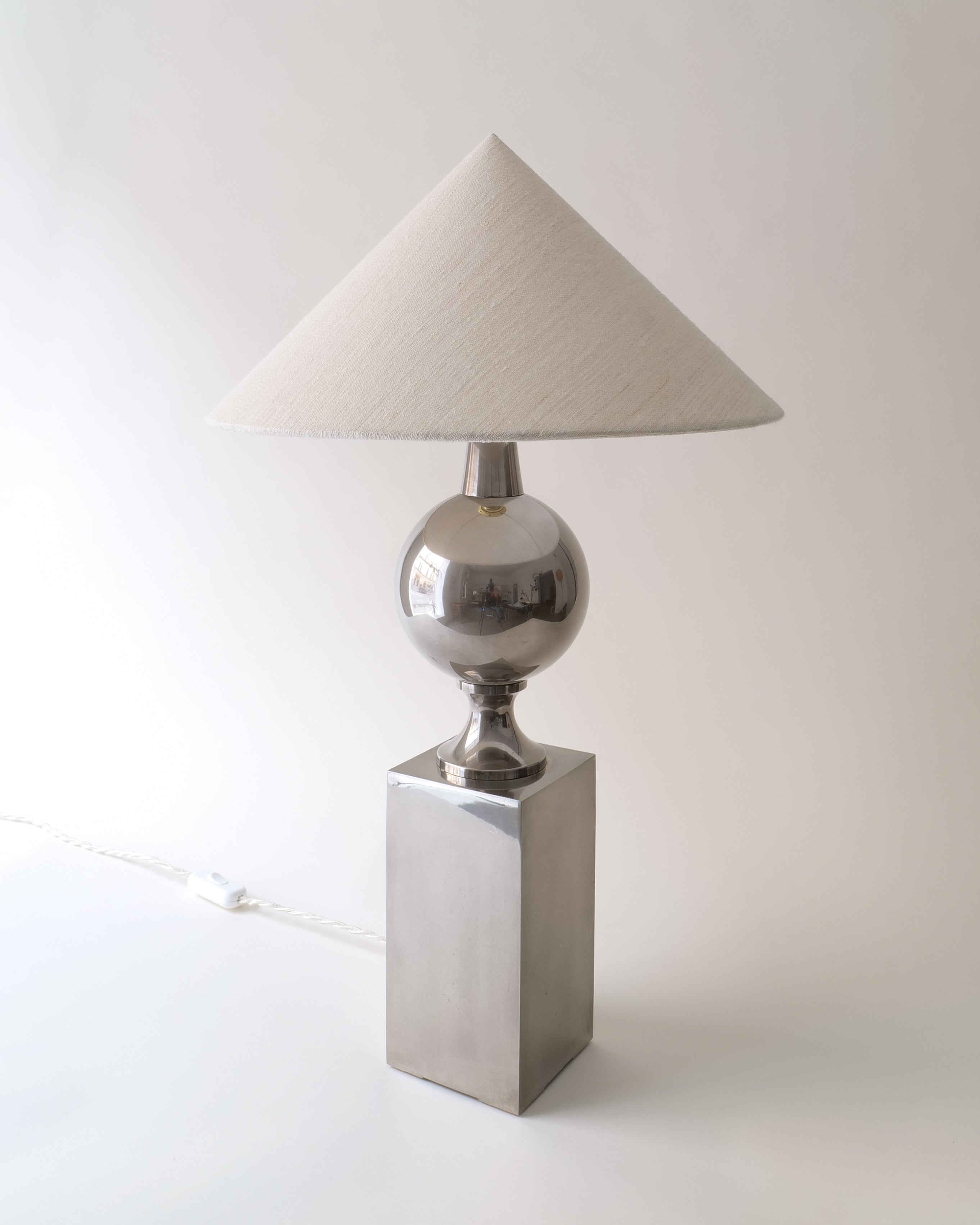 Table lamp with a silver metallic base and white lampshade on a light background