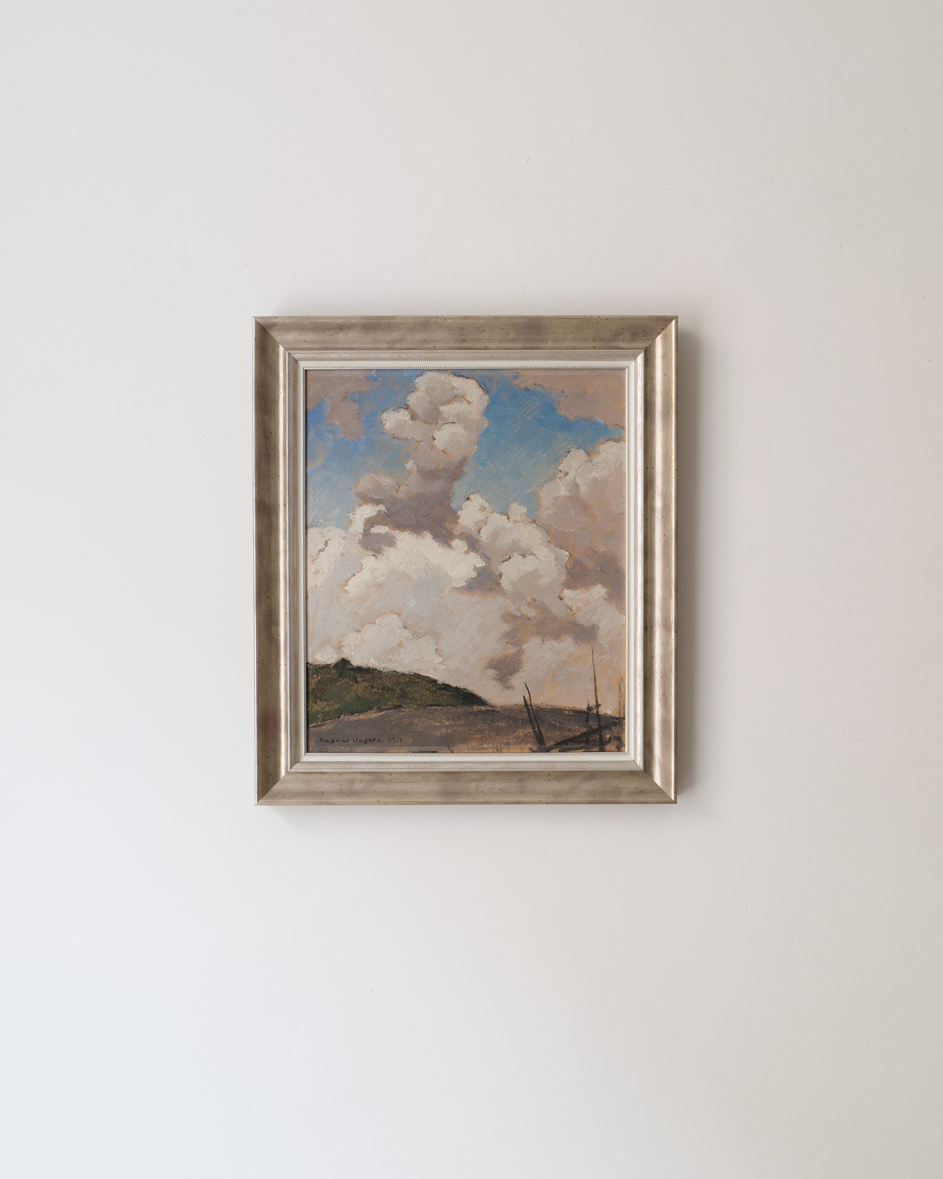 Framed painting of a landscape with clouds on a white wall