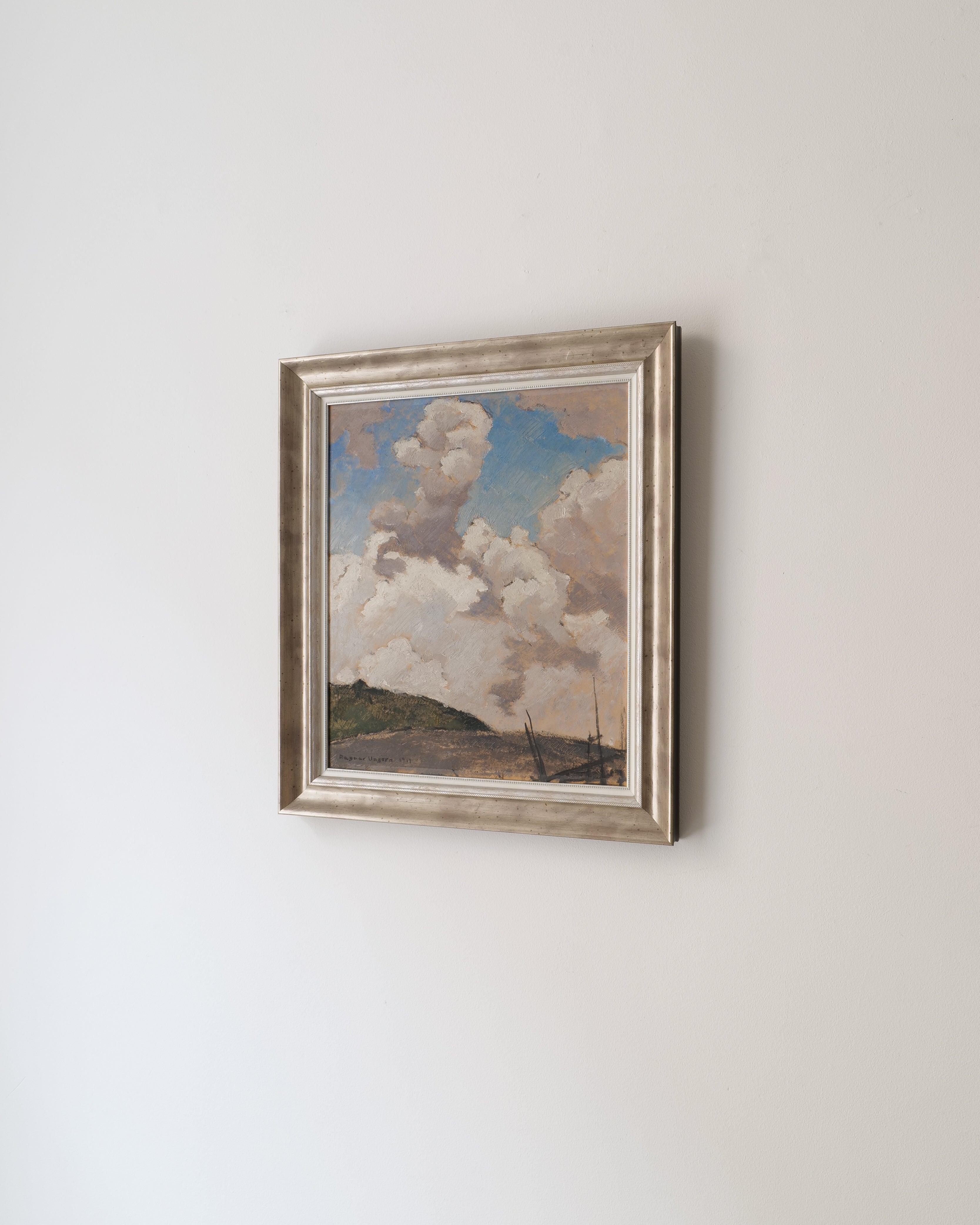 Framed artwork of a landscape with clouds on a white wall