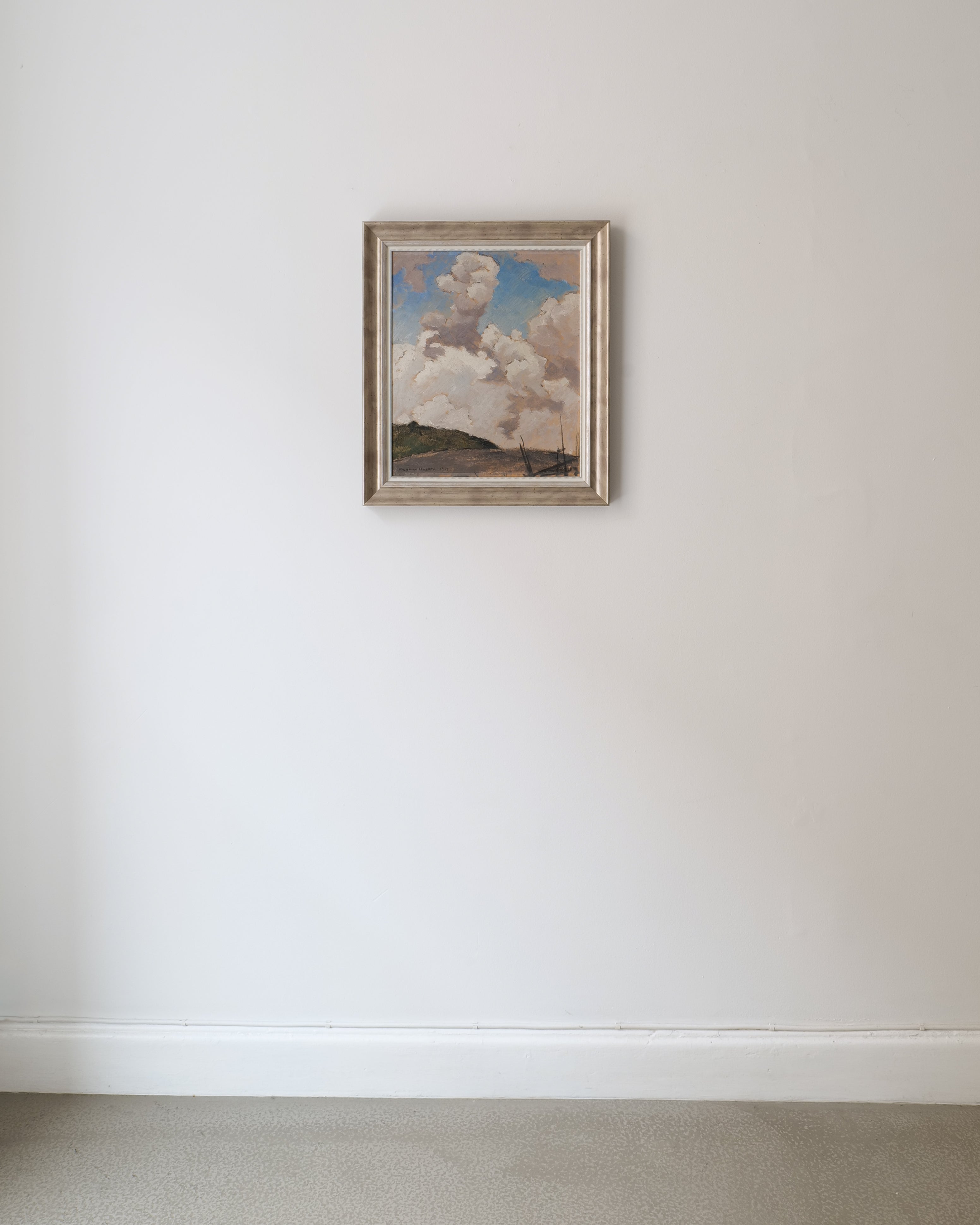 Framed artwork of a landscape with clouds on a white wall.