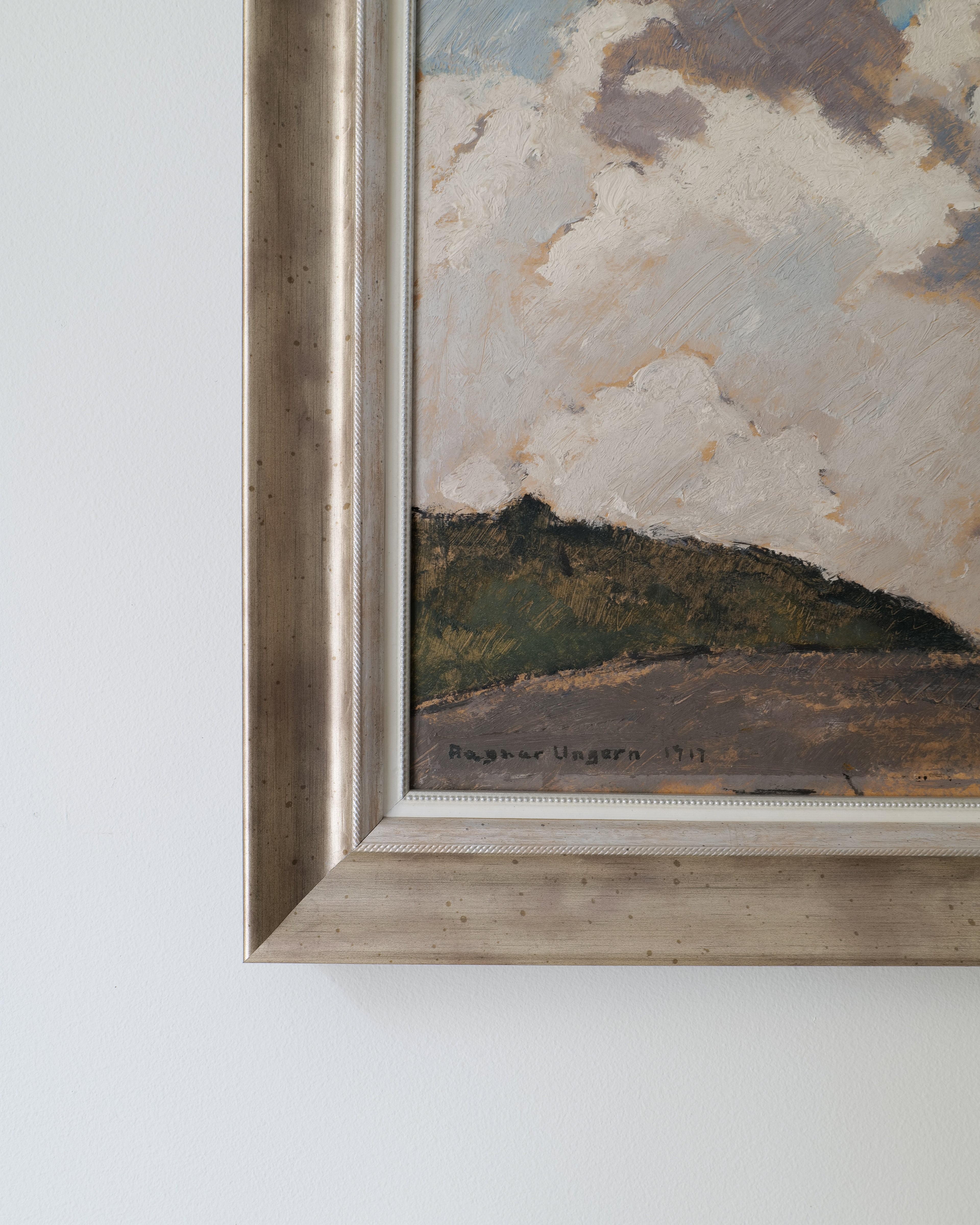 Framed painting of a landscape with clouds on a white wall