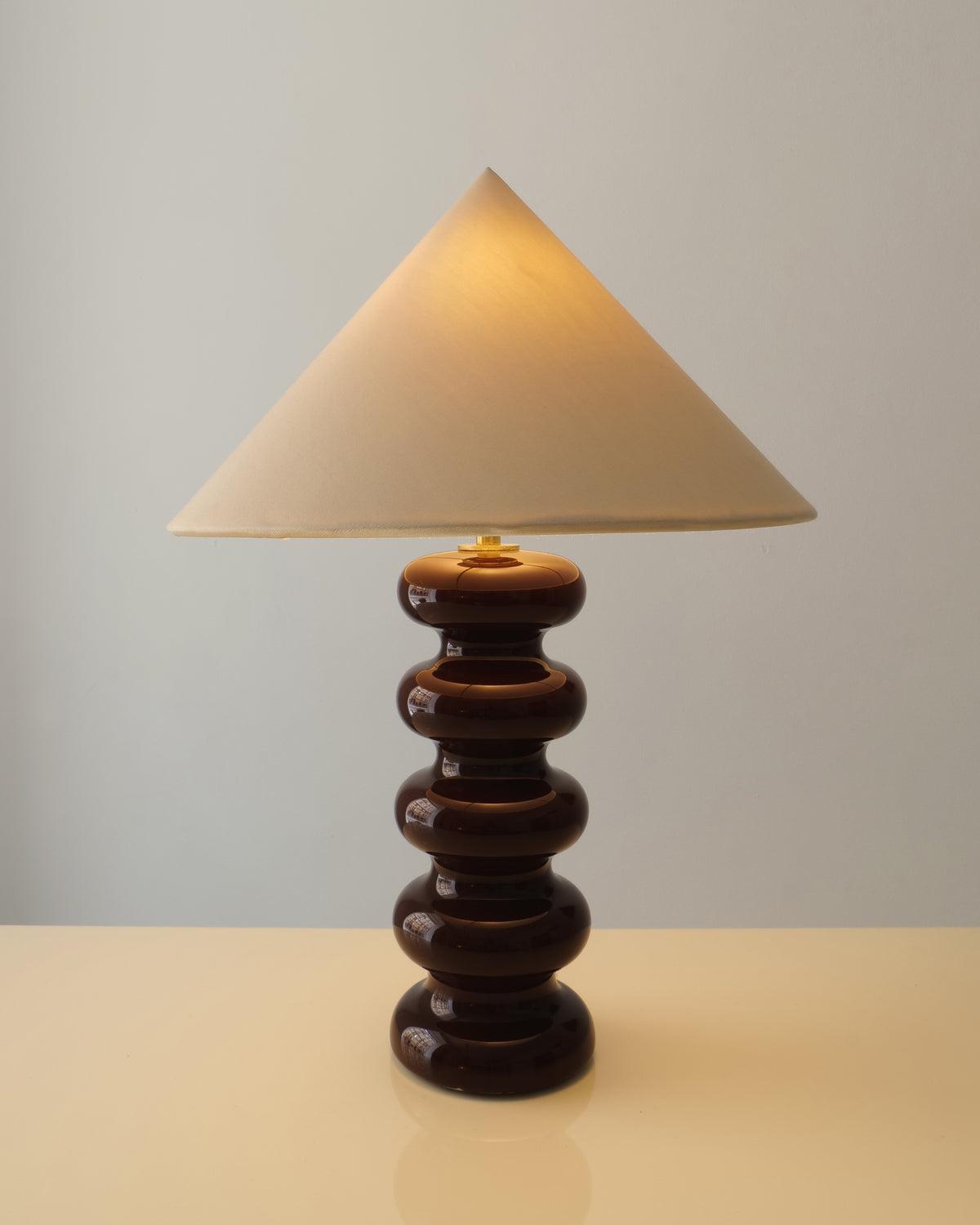 Doulton stacked sphere ceramic table lamp 1970s, bitter chocolate glaze with ivory conical shade, full view lit in warm setting.