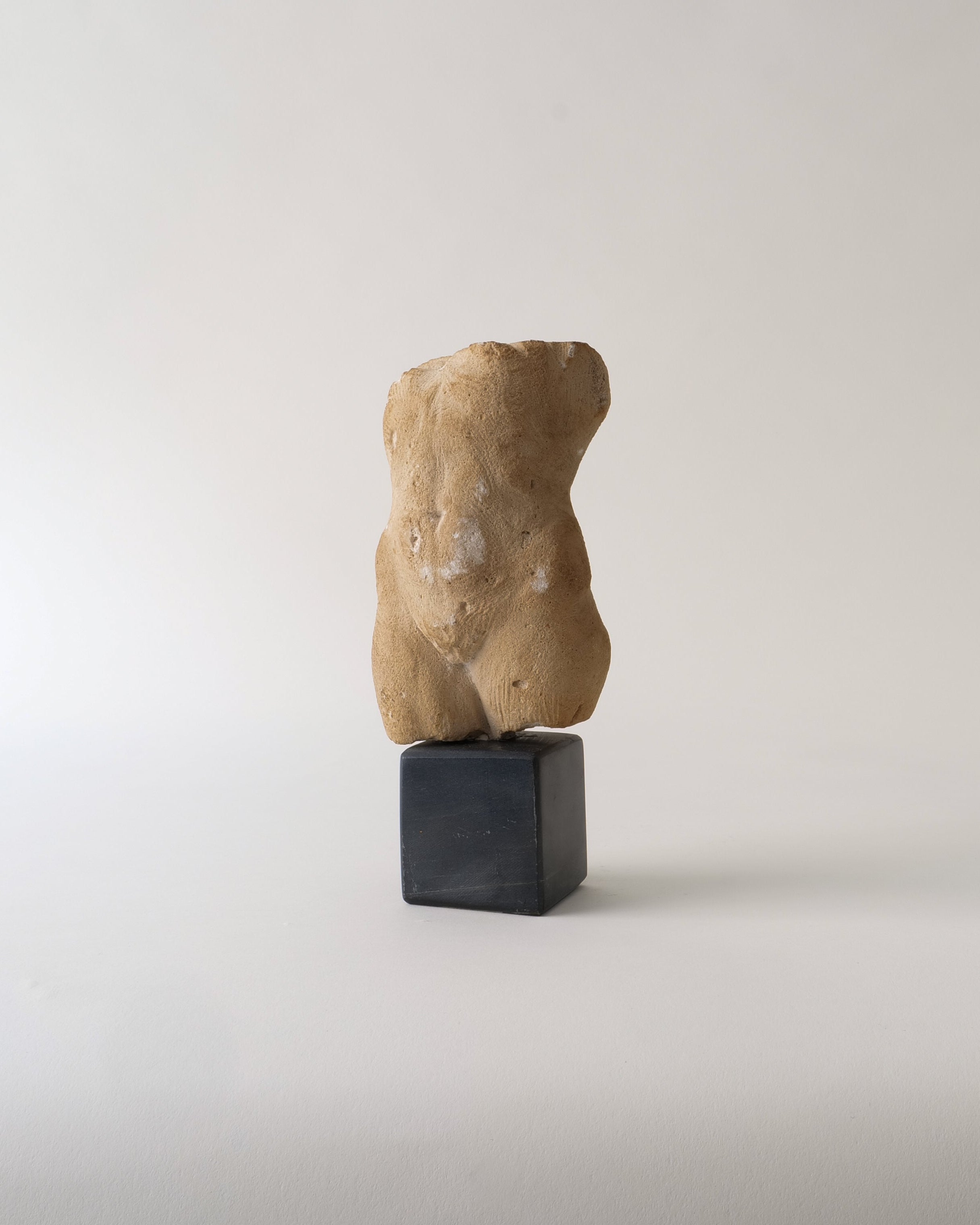 Stone sculpture of a torso on a black pedestal against a white background