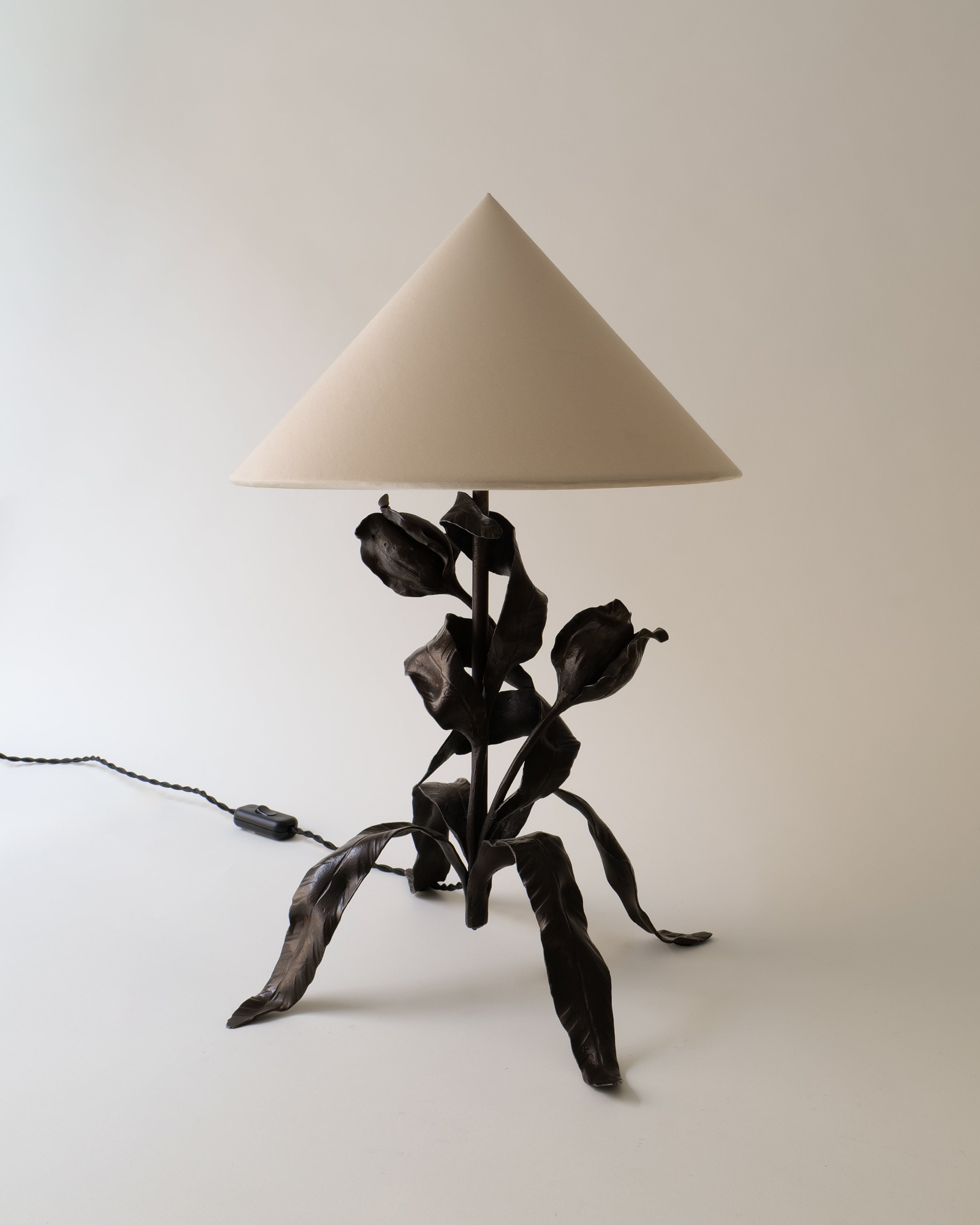 Art Nouveau table lamp with black metal base shaped like leaves on a white background
