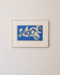 Framed Japanese wood block printed artwork of a floral blossom design on a blue background, mounted on a beige wall.
