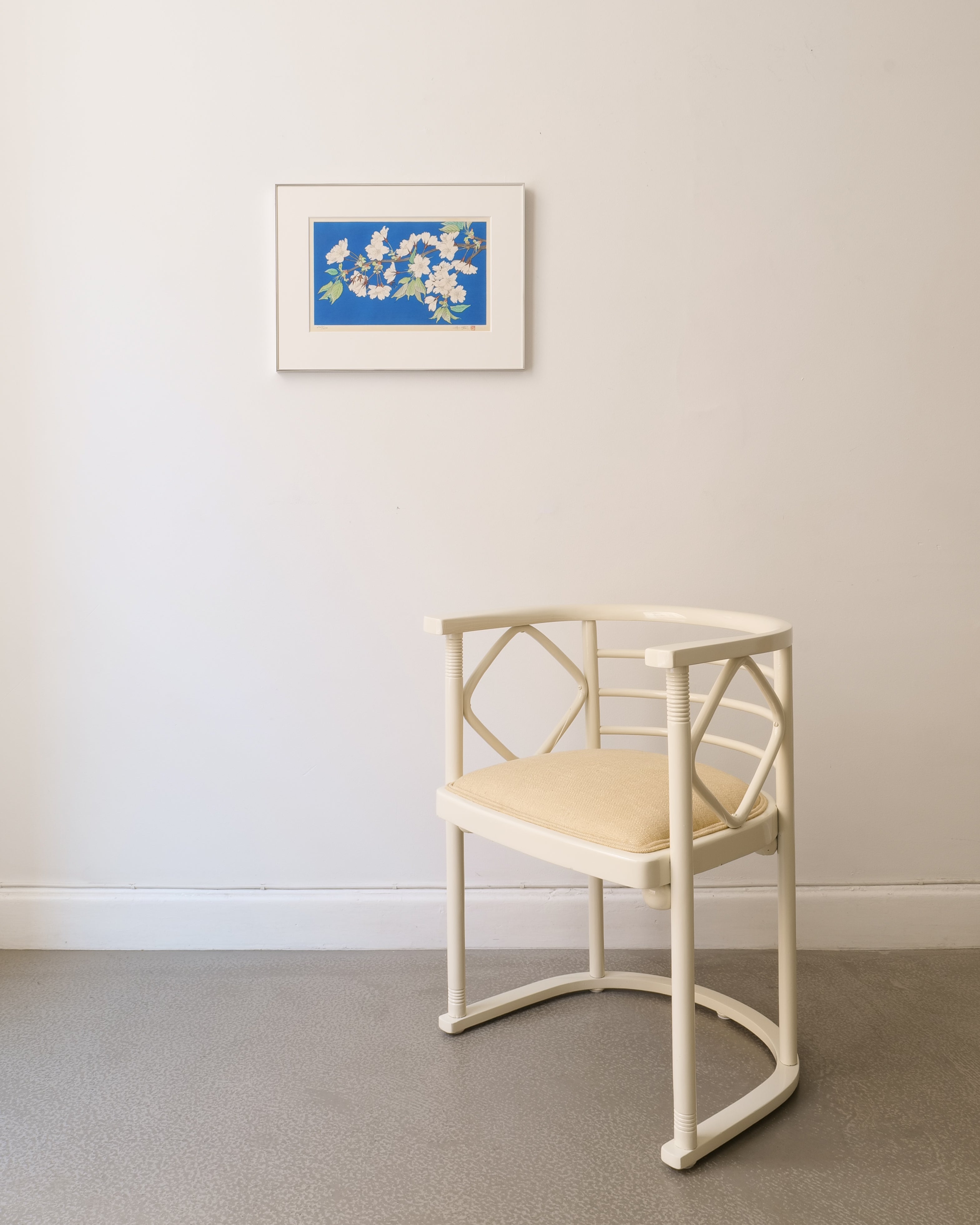 Framed Japanese wood block printed artwork of a floral blossom design on a blue background, mounted on a beige wall with Josef Hoffman off white lacquered chair in foreground